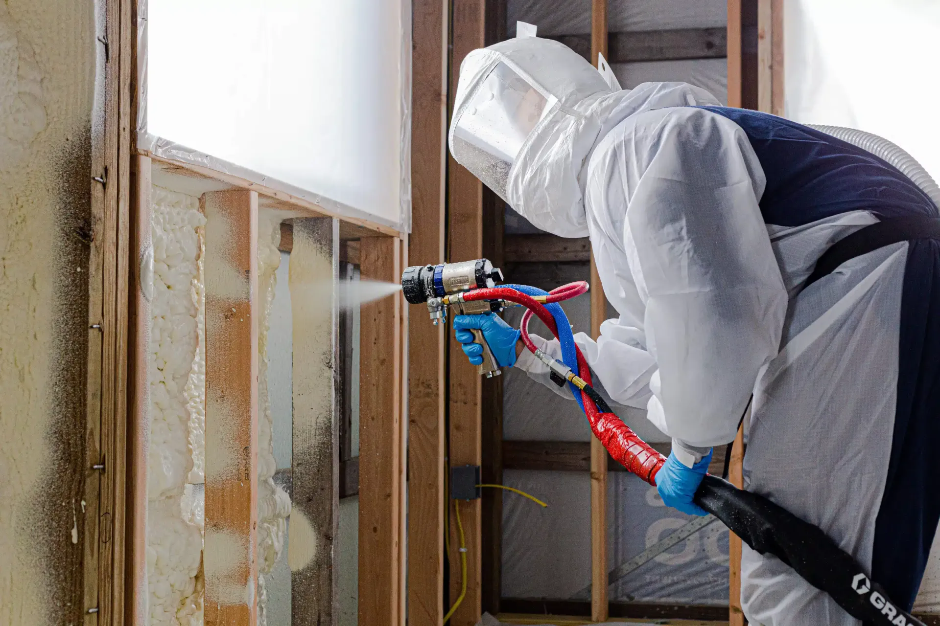 technician-wearing-protective-gear-spraying-polyurethane-insulation-into-open-wall-studs
